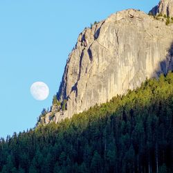 Low angle view of moon on mountain against clear blue sky