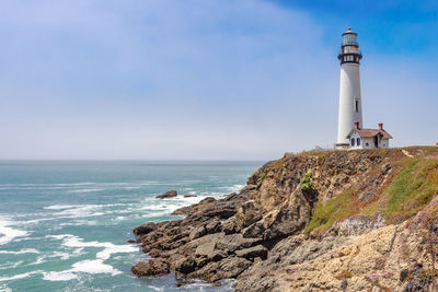 Lighthouse by sea against sky