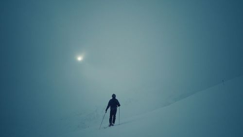 Silhouette person skiing on snow covered landscape against sky at night