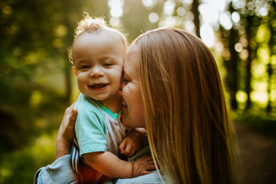 Happy mom snuggling baby boy outside in forest