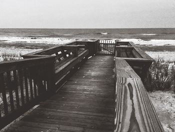 Empty wooden chairs at beach against sky