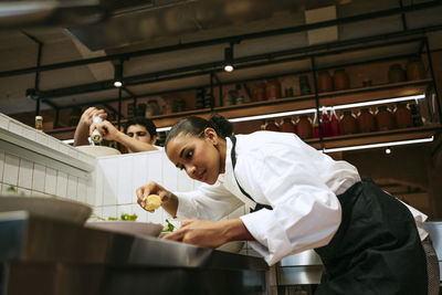 Low angle view of female chef squeezing lemon on salad with male coworker seasoning at commercial kitchen
