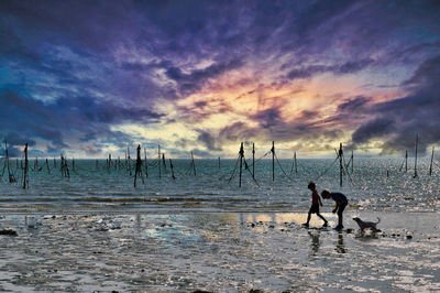 Silhouette people on beach against sky during sunset