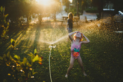 A young girl wearing bathing suit playing on the grass with sprinkler
