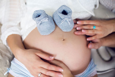 Hands of their parents, dressed in white, holding a knitted blue booties boy newborn