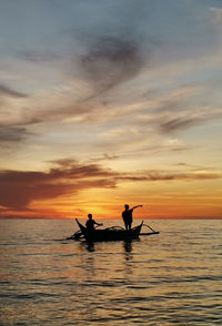 Silhouette people in sea against sky during sunset