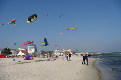 Colorful kites flying over people at beach against clear sky