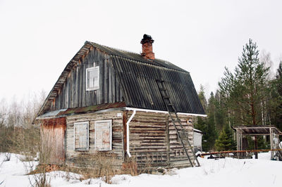 Abandoned house on snow covered field against sky