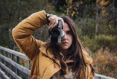 Portrait of young woman taking photos of beautiful autumn nature with a vintage film camera