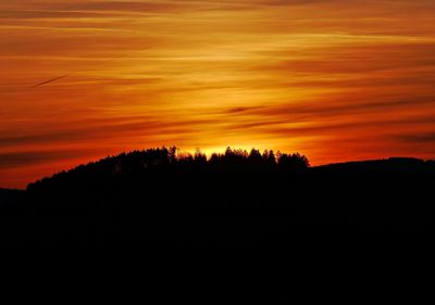 Silhouette trees on landscape against dramatic sky during sunset