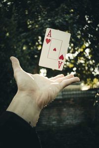 Cropped hand of man with levitating card against tree