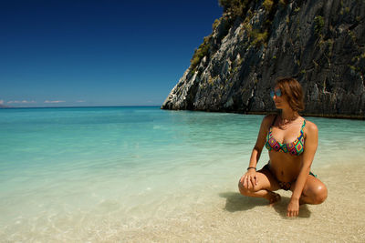 Rear view of young woman on beach against clear blue sky