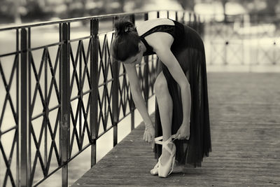 Young ballet dancer tying shoe on boardwalk