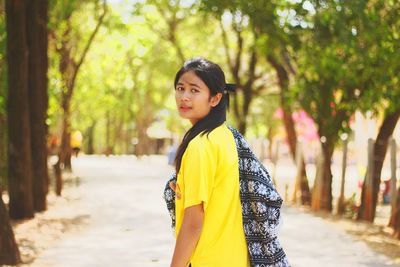 Portrait of young woman standing on road against trees