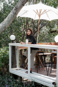 Portrait of woman sitting on seat against trees