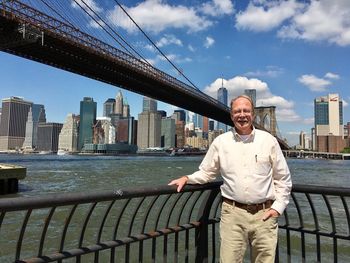 Portrait of senior man standing against brooklyn bridge and one world trade center