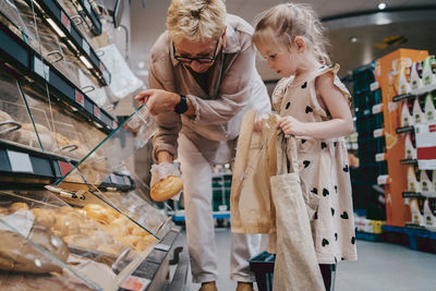 Senior woman buying bread with granddaughter holding bags at grocery store