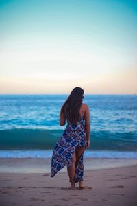 Rear view full length of woman standing at beach during sunset