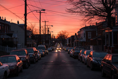 Cars on street in city against sky at sunset