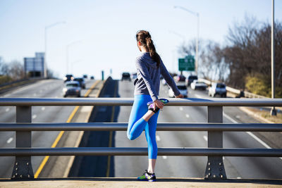 Rear view of woman exercising on footpath against clear sky in city