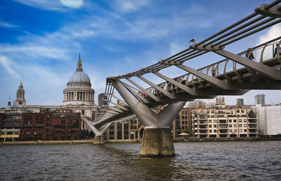 Bridge over river by buildings against sky in city