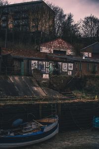 Boats moored in house by trees against sky