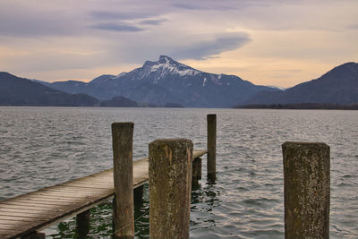 Wooden posts on snowcapped mountains by lake against sky