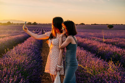 Women taking selfie while standing on field against sky during sunset