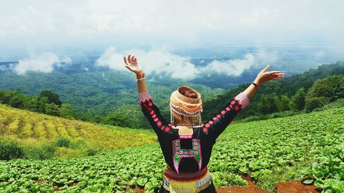 Rear view of woman with arms raised standing against landscape against sky