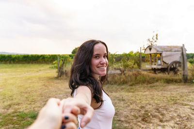 Portrait of smiling young woman standing on field against sky