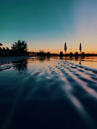 Silhouette swimming pool by lake against sky during sunset