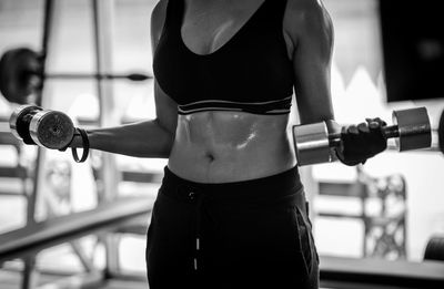 Midsection of woman holding dumbbells and exercising at gym 