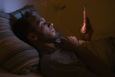 Side view of man using smart phone while lying on bed at home