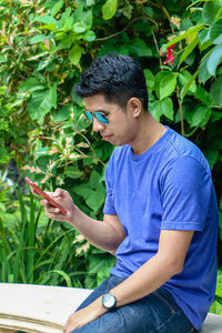 Man using phone while sitting by plants