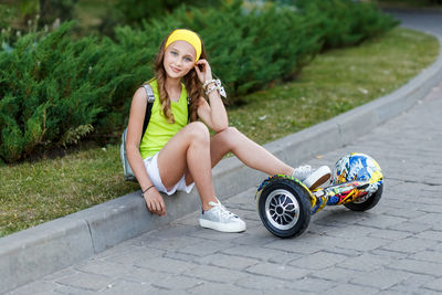 Full length portrait of teenage girl with hoverboard sitting at park