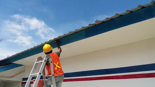 Low angle view of worker working against blue sky