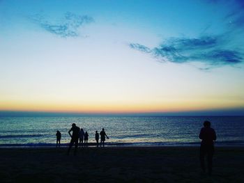 Silhouette people on beach against sky during sunset