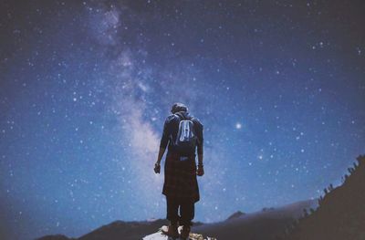 Rear view of man standing on rock against sky at night