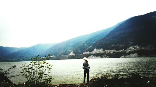 Rear view of woman standing on lake against mountains