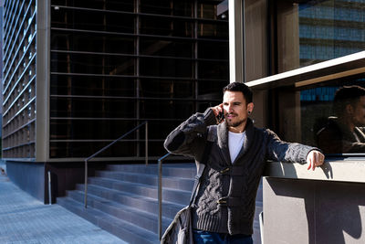 Man using smartphone outdoors, standing next to office building