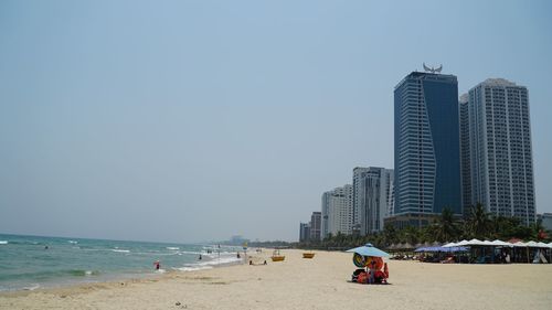People on beach by buildings against clear sky