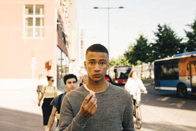 Portrait of teenage boy holding food while walking on street in city