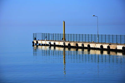 Pier on sea against clear blue sky