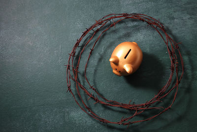 High angle view of rusty barbed wire with piggy bank on blackboard