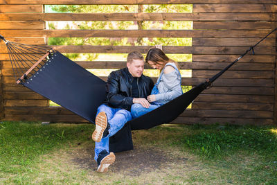 Couple sitting on hammock by wooden wall