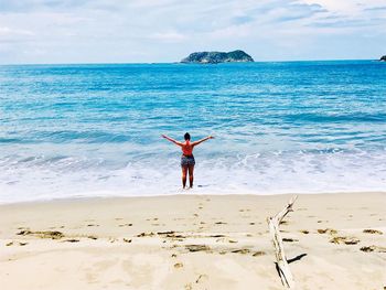 Rear view of woman with arms outstretched standing at beach