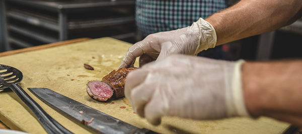 Cropped hands of chef wearing gloves while preparing meat in kitchen