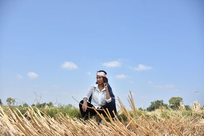 Woman crouching on field against blue sky