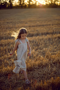Girl child with long hair walking across the field wearing with long hair during sunset