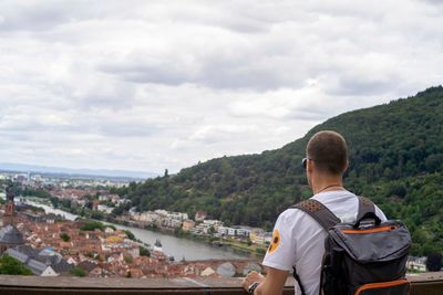 Rear view of man looking at cityscape against sky